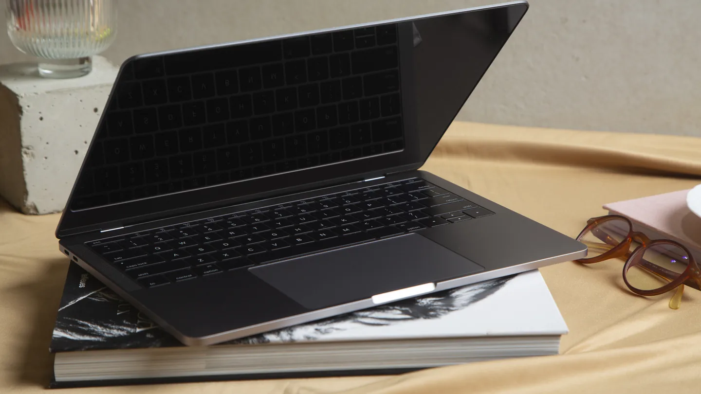 Dunne laptop met een donker scherm, open op een stapel boeken naast een bril