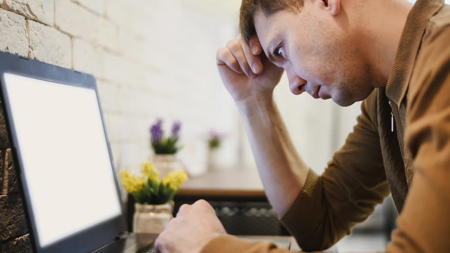 Man met zijn hoofd in zijn hand kijkt naar een laptop met een leeg scherm