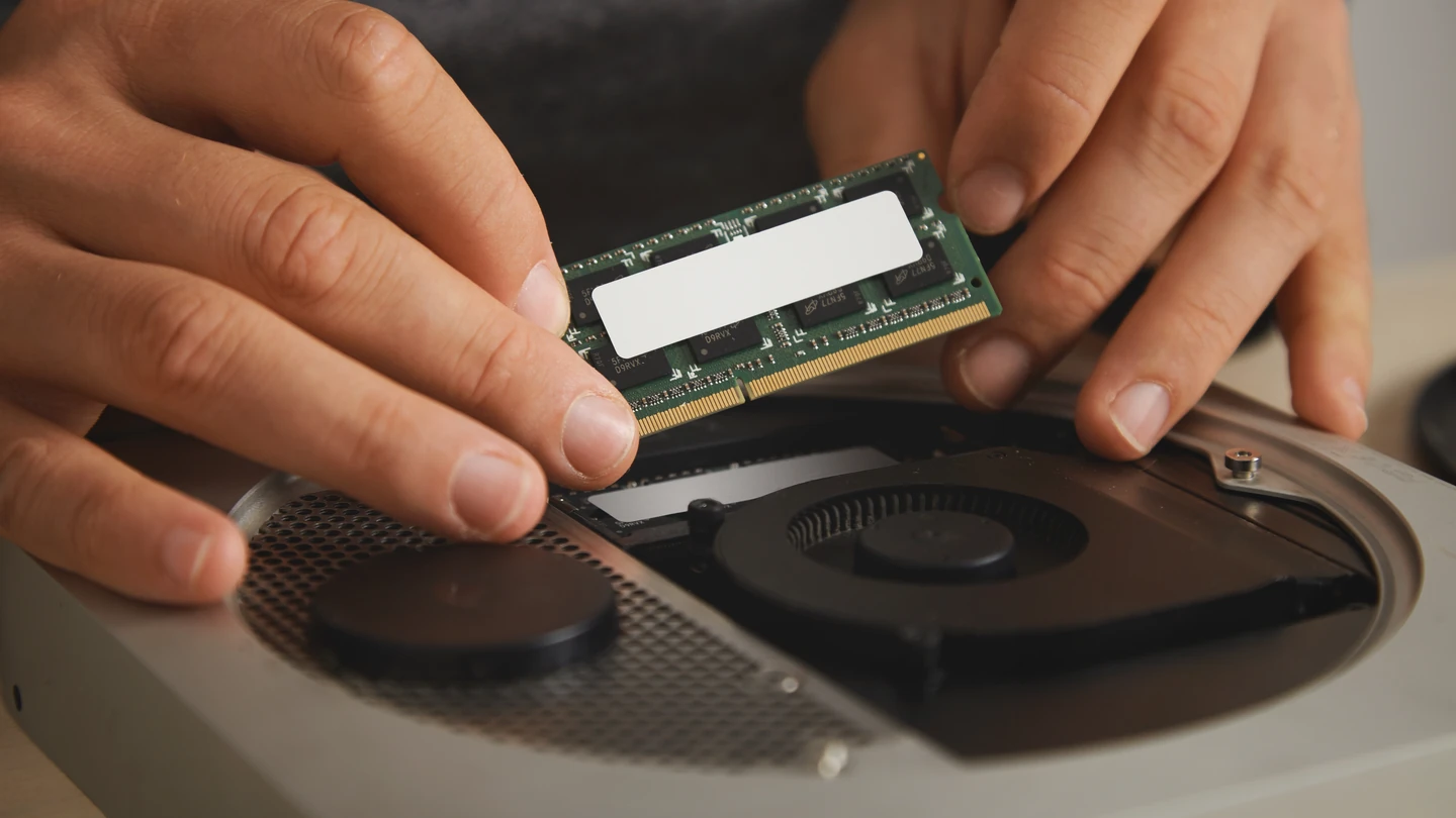 Twee handen plaatsen een geheugenmodule in een geopende laptop